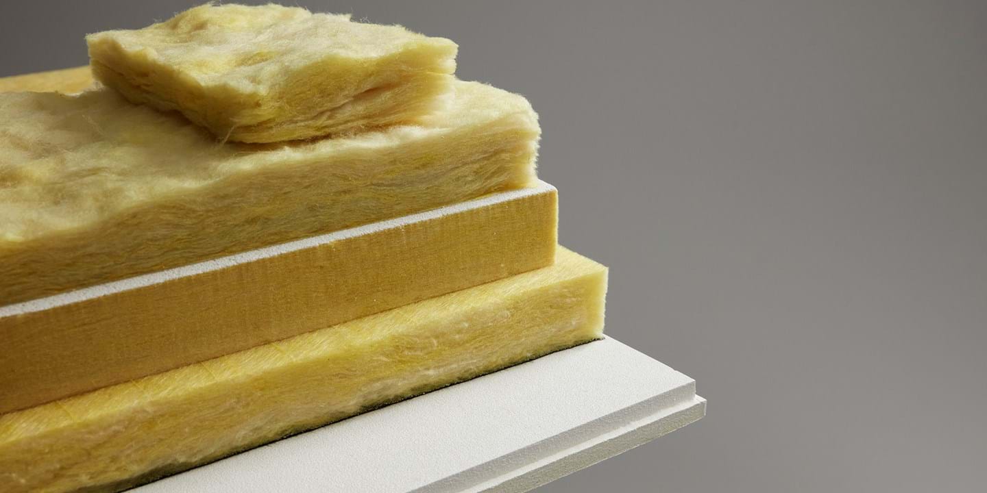 A stack of yellow glass wool panels in various thicknesses is displayed on a white surface against a grey background. The panels have a fluffy texture, highlighting the materials absorbing properties.