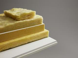 A stack of yellow glass wool panels in various thicknesses is displayed on a white surface against a grey background. The panels have a fluffy texture, highlighting the materials absorbing properties.