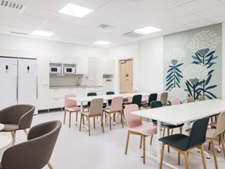 Valkoinen, akustinen alakatto sairaalan henkilökunnan ruokasalissa valkoisin ja pastellivärisin kalustein. Oikealla seinällä näkyy suuri seinäkoristelu, jossa on suuria kukkia.