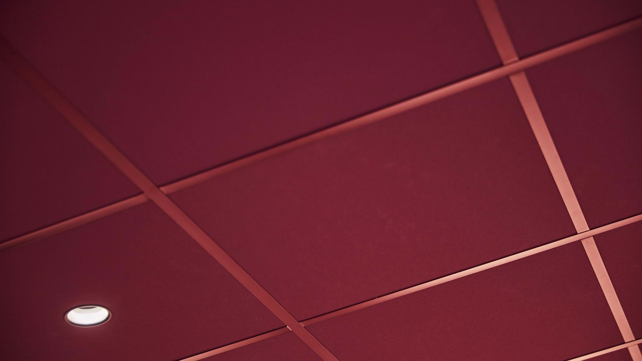 Närbild av mörkrött akustiskt undertak med matchande bärverk