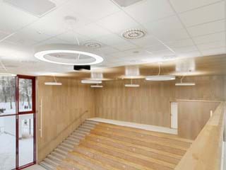 A modern, open interior with tiered wooden seating, high ceilings, and circular ceiling lights. Large windows offer natural light, with a snowy landscape visible outside.