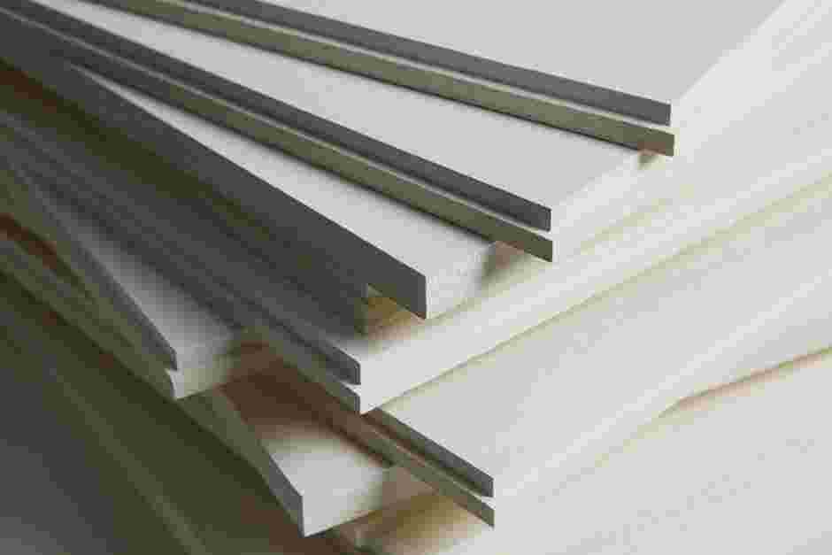 A close-up of multiple white acoustic boards stacked on top of each other, showing their thin edges and layered arrangement. The smooth surfaces and precise cuts are visible, creating a geometric pattern.