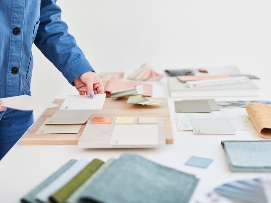 Partly visible person dressed in blue standing at a table with colour samples in pastel colours