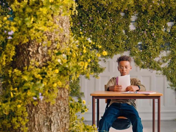 Boy reading a book at school desk in room with plants growing on the walls