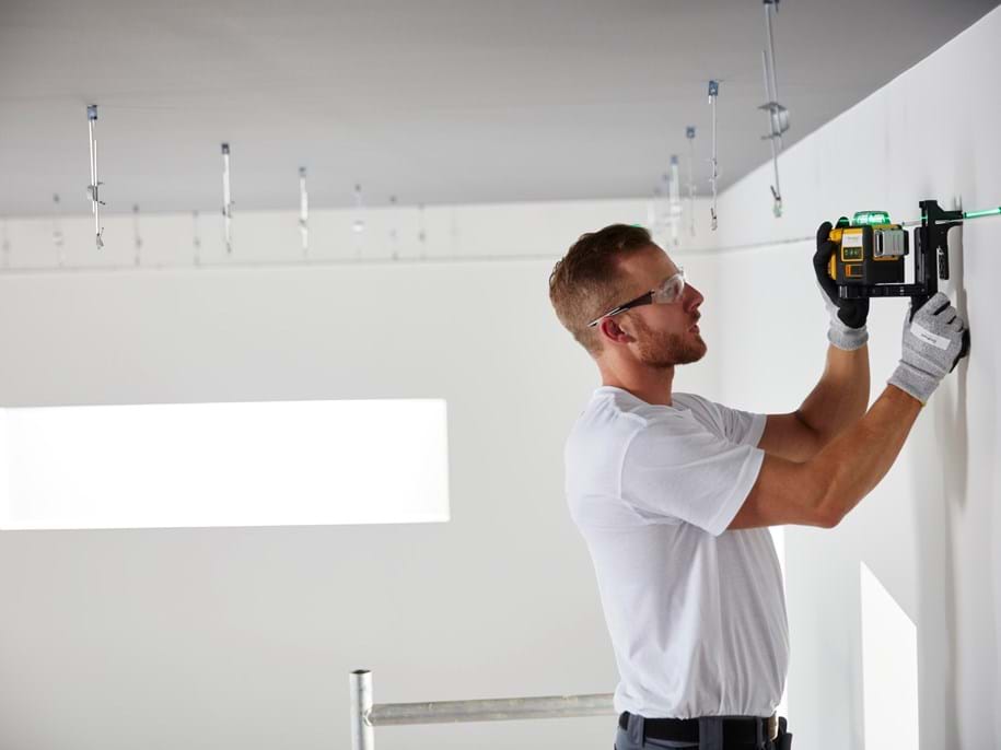 Uzstādītājs mēra tukšu telpu, gatavojas griestu uzstādīšanai