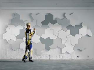 Woman in colourful dress standing in front of a concrete wall covered with white and grey acoustic wall panels in jigsaw pattern