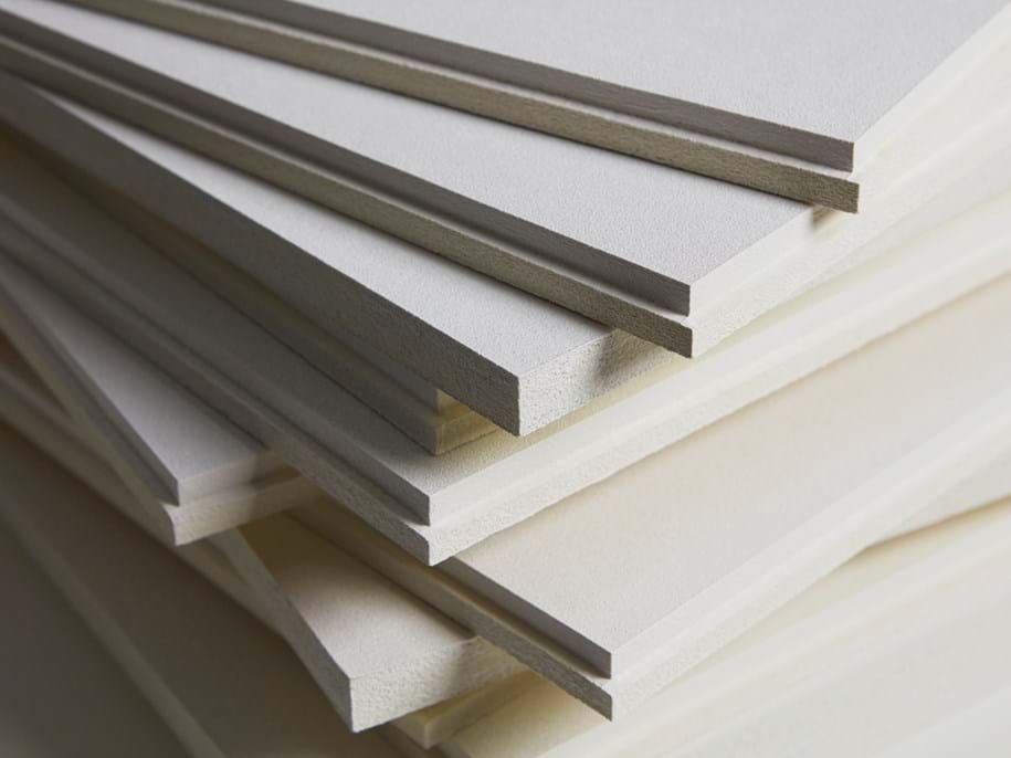 A close-up view of a stack of rectangular, white acoustic panels with smooth edges. The panels are arranged in a slightly staggered manner, displaying the thickness and texture of the material. The background is blurred.