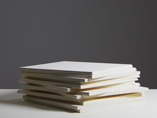 A pile of white acoustic panels lying on a white surface and a dark grey background
